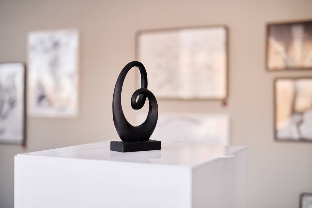 Abstract black sculpture on a pedestal in front of framed artworks
