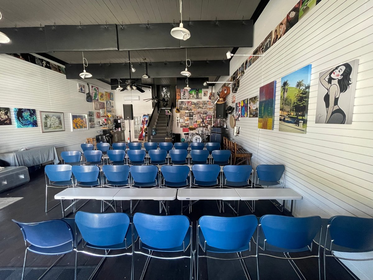 Inside the studio with rows of blue chairs arranged for a seated event, surrounded by artwork on the walls