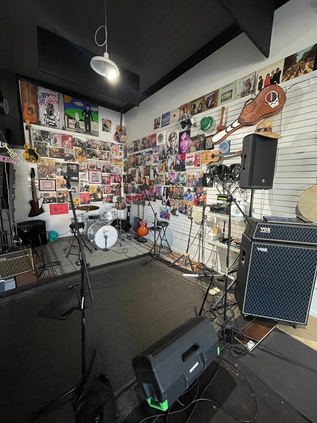 Rehearsal space at the studio with a drum kit, amplifiers, guitars, and a wall covered in music posters